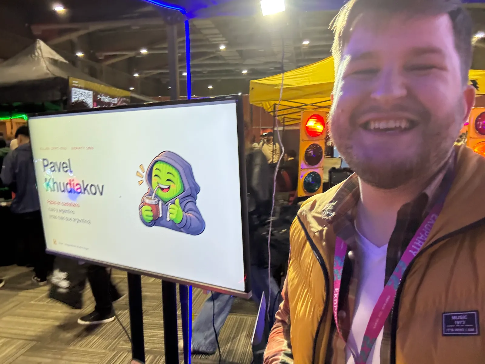 The author, smiling, in a conference hall next to a screen showing the title slide of the talk: his name and a green hooded sticker character holding a mate gourd.